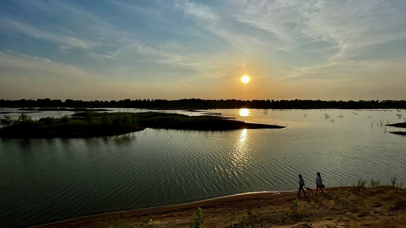 Picha iliyopigwa kwa simu ya mkononi ikionyesha watu wakitembea kwa kufuata kando ya Mto Yongding wakati wa machweo ya jua katika Eneo la Daxing, Beijing, China, Mei 30, 2021. (Xinhua/Li Xin)