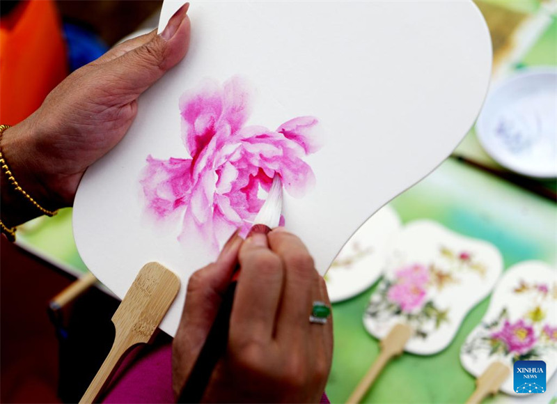 Mfanyakazi akichora feni ya mkononi yenye kauli mbiu ya maua peony kwenye bustani ya mimea huko Luoyang, Mkoa wa Henan, Katikati ya China, Aprili 17, 2024.  (Xinhua/Li Jianan)