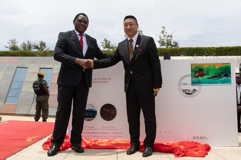 Rais wa Zambia Hakainde Hichilema (kushoto) na Balozi wa China nchini Zambia Han Jing wakipeana mikono baada ya kuzindua bahasha ya kumbukumbu ya maadhimisho ya miaka 60 ya uhusiano wa kidiplomasia kati ya China na Zambia yaliyofanyika katika Eneo la Kumbukumbu ya Reli ya Tanzania na Zambia (TAZARA) wilayani Chongwe, Lusaka, Zambia. Oktoba 29, 2024. (Xinhua/Peng Lijun)