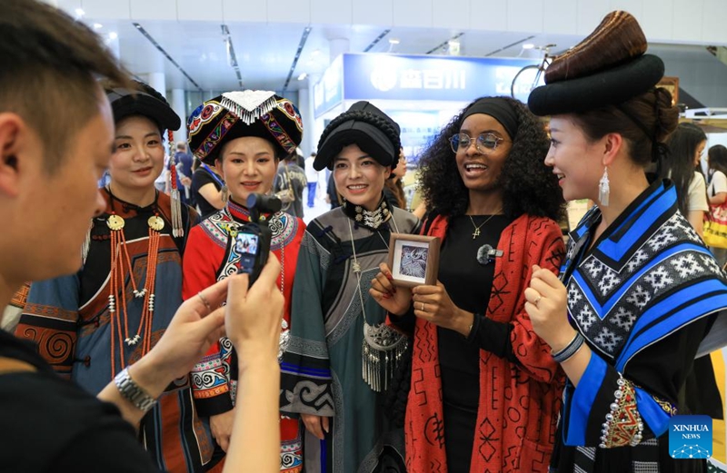 Mshiriki wa kigeni akirekodi video na washiriki kutoka makabila ya Wamiao na Wayi kwenye Maonyesho ya 22 ya Kimataifa ya Mambo ya Utamaduni ya China, Shenzhen, Mkoa wa Guangdong, kusini mwa China, Mei 21, 2026. (Xinhua/Mao Siqian)