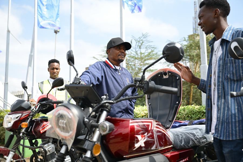 Mtembeleaji (katikati) akimuuliza mwonyeshaji bidhaa kuhusu pikipiki iliyotengenezwa China kwenye Maonyesho ya Kimataifa ya Mashine za Ujenzi ya Afrika 2026 jijini Nairobi, Kenya, Juni 19, 2026. (Xinhua/Yang Guang)